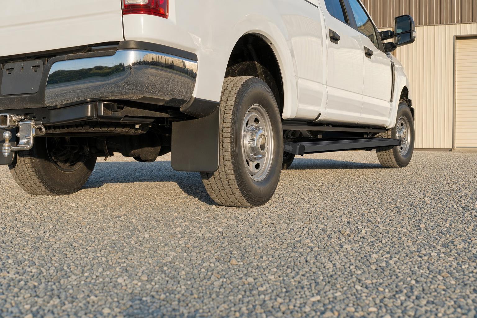 Low view of black running boards, a mud flap, and a hitch on a white pickup